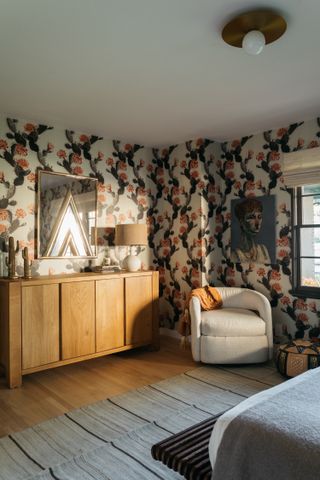 A bedroom with a wall covered in wallpaper, and a console kept in front with a mirror above