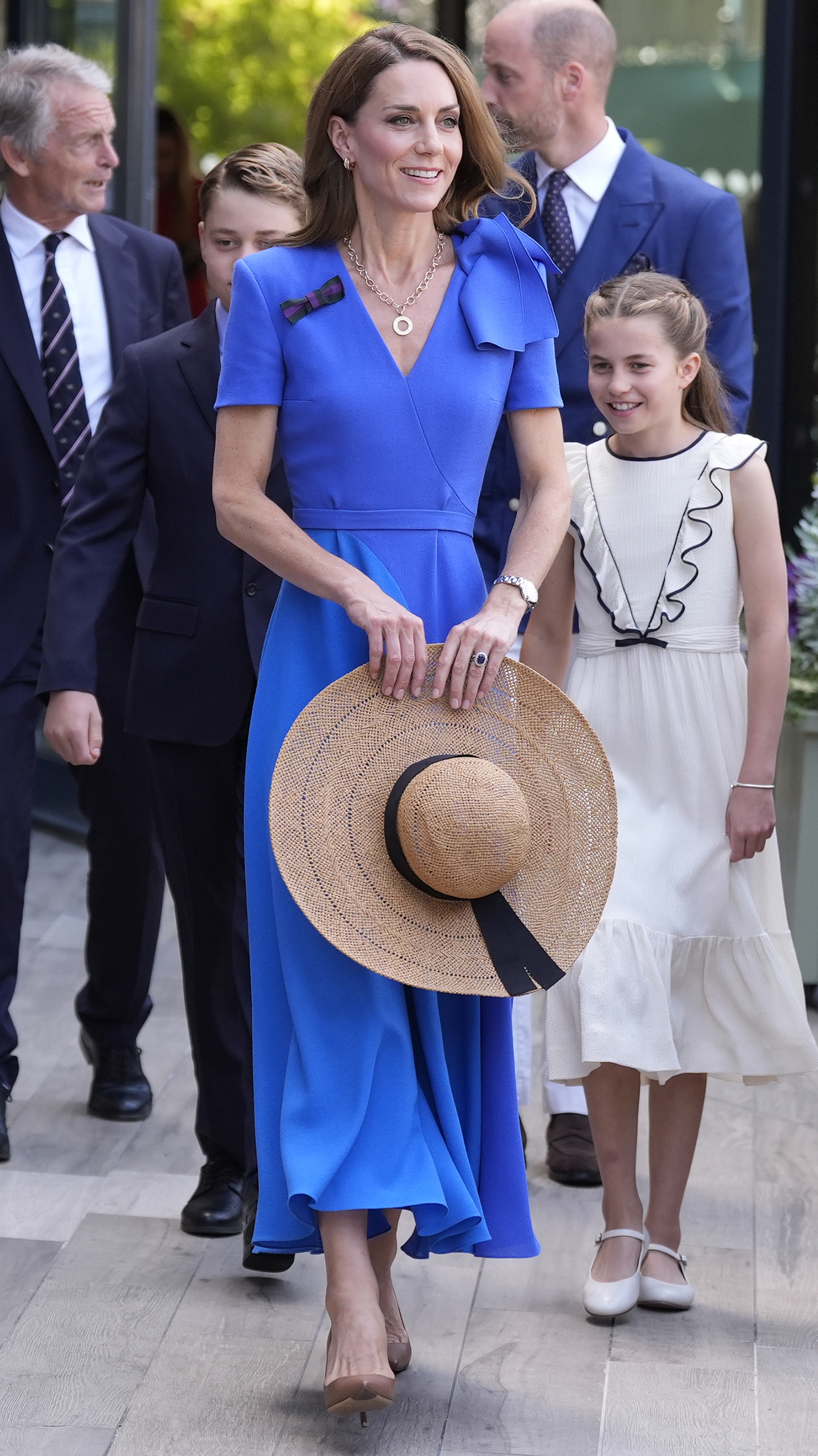 Catherine, Princess of Wales walks holding a sunhat, accompanied by Prince George, Princess Charlotte and William, Prince of Wales on day fourteen of The Championships Wimbledon 2025