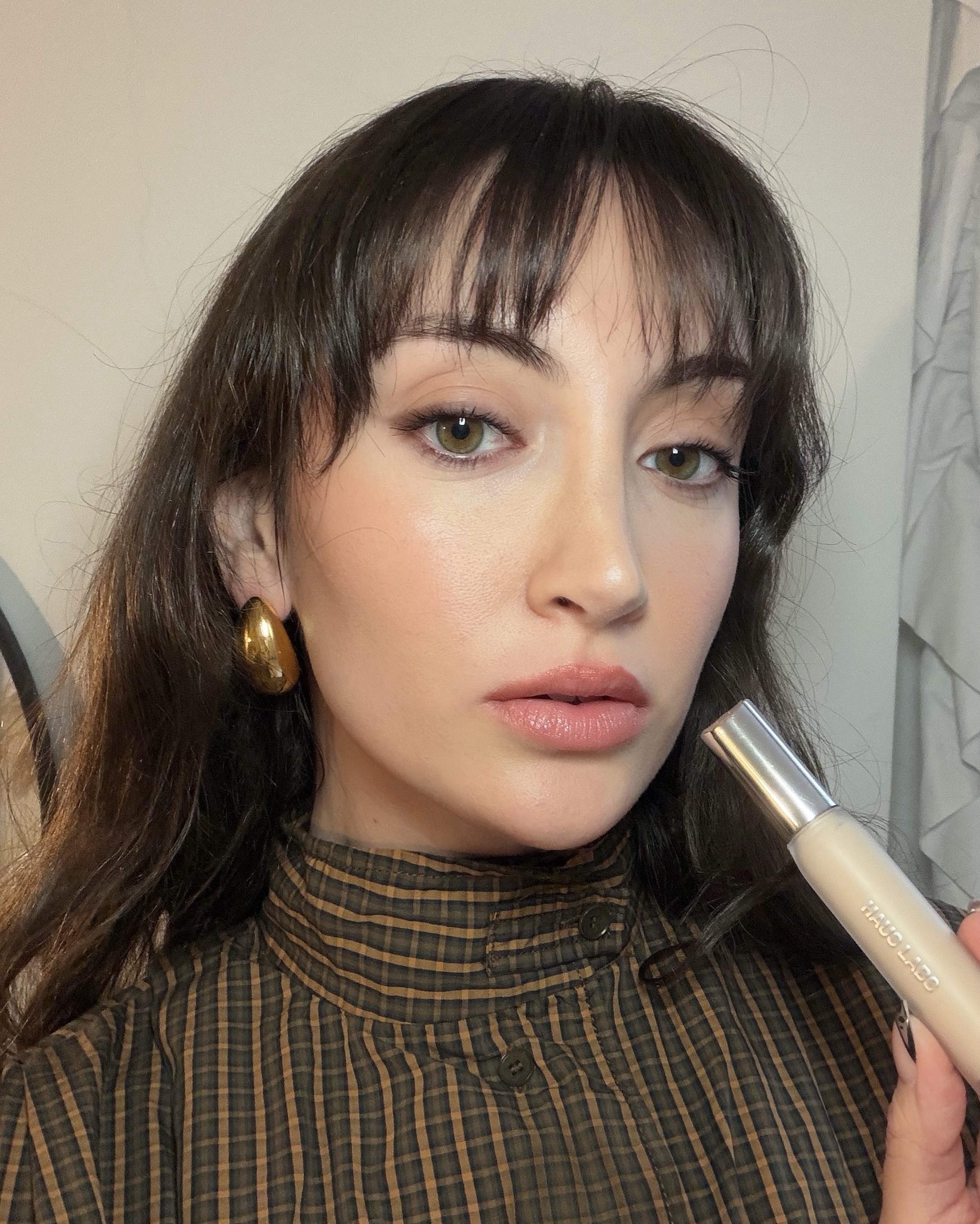 An image ofBest Knockoff Luxury Clothing
 associate beauty editor Alyssa Brascia wearing and holding the Haus Labs Triclone Skin Tech Concealer.