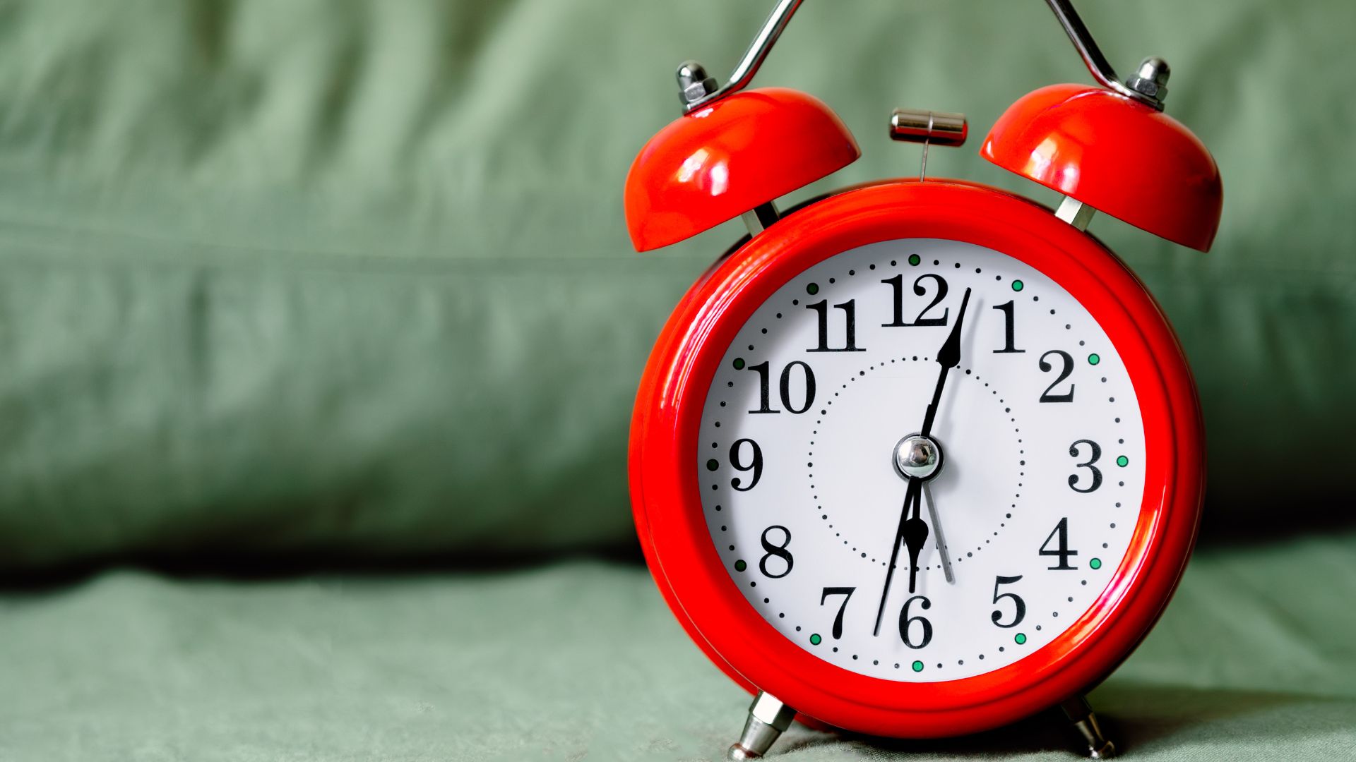A red alarm clock placed on a light gray/green bed.