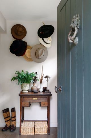 blue front door open to entryway with hats on pegs and country boots with small side table