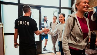 People entering gym greeted by a man with Coach written on the back of his T-shirt