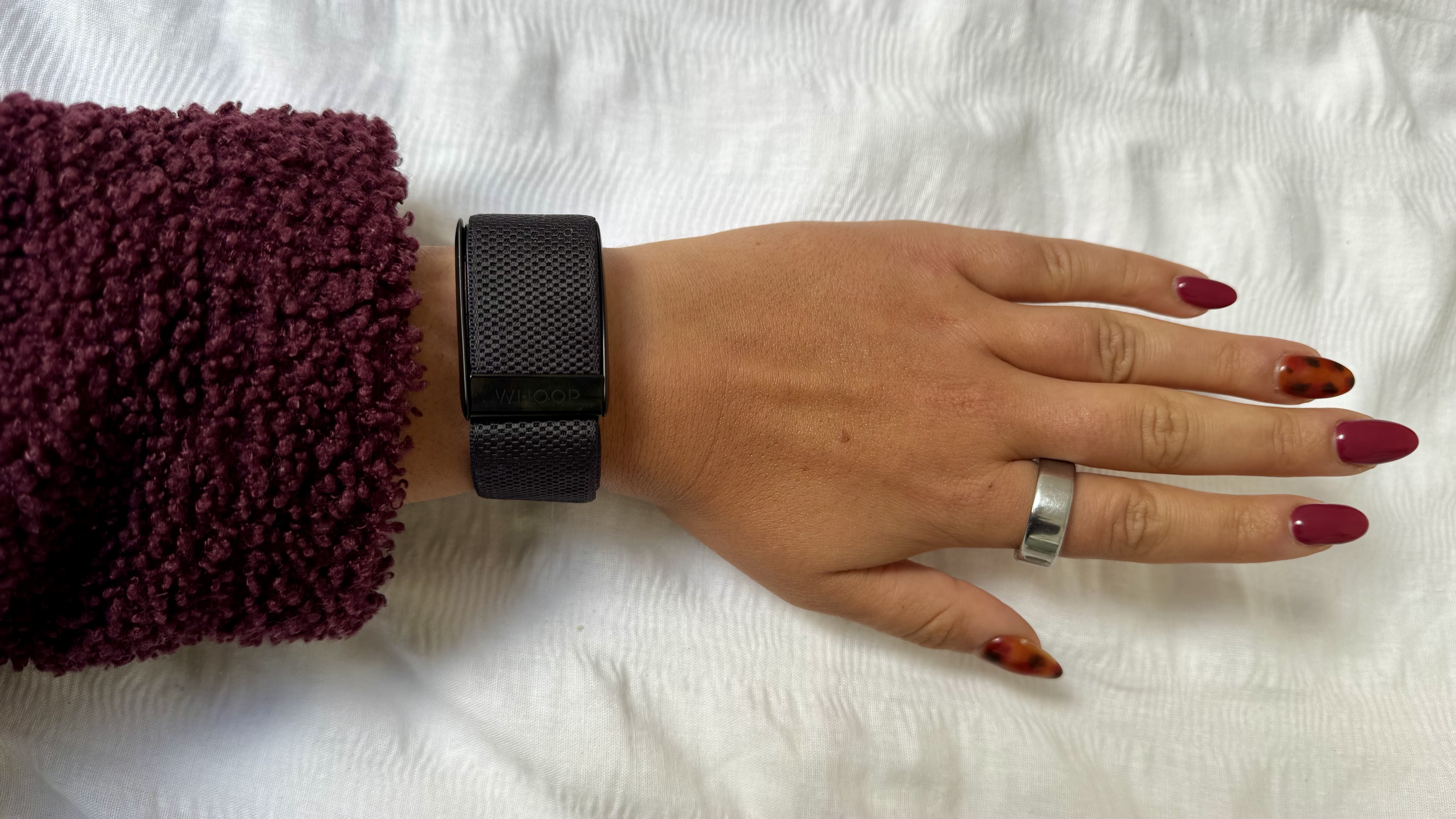 A woman&#039;s hand wearing a silver Oura Ring 4 on index finger and a black Whoop MG on wrist