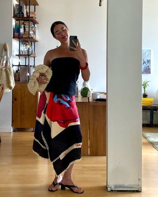 Fashion influencer wearing a black strapless top, printed asymmetric midi skirt, and heeled thong sandals.