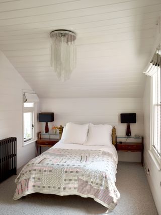 Small white panelled bedroom with modern chandelier and traditional bedspread