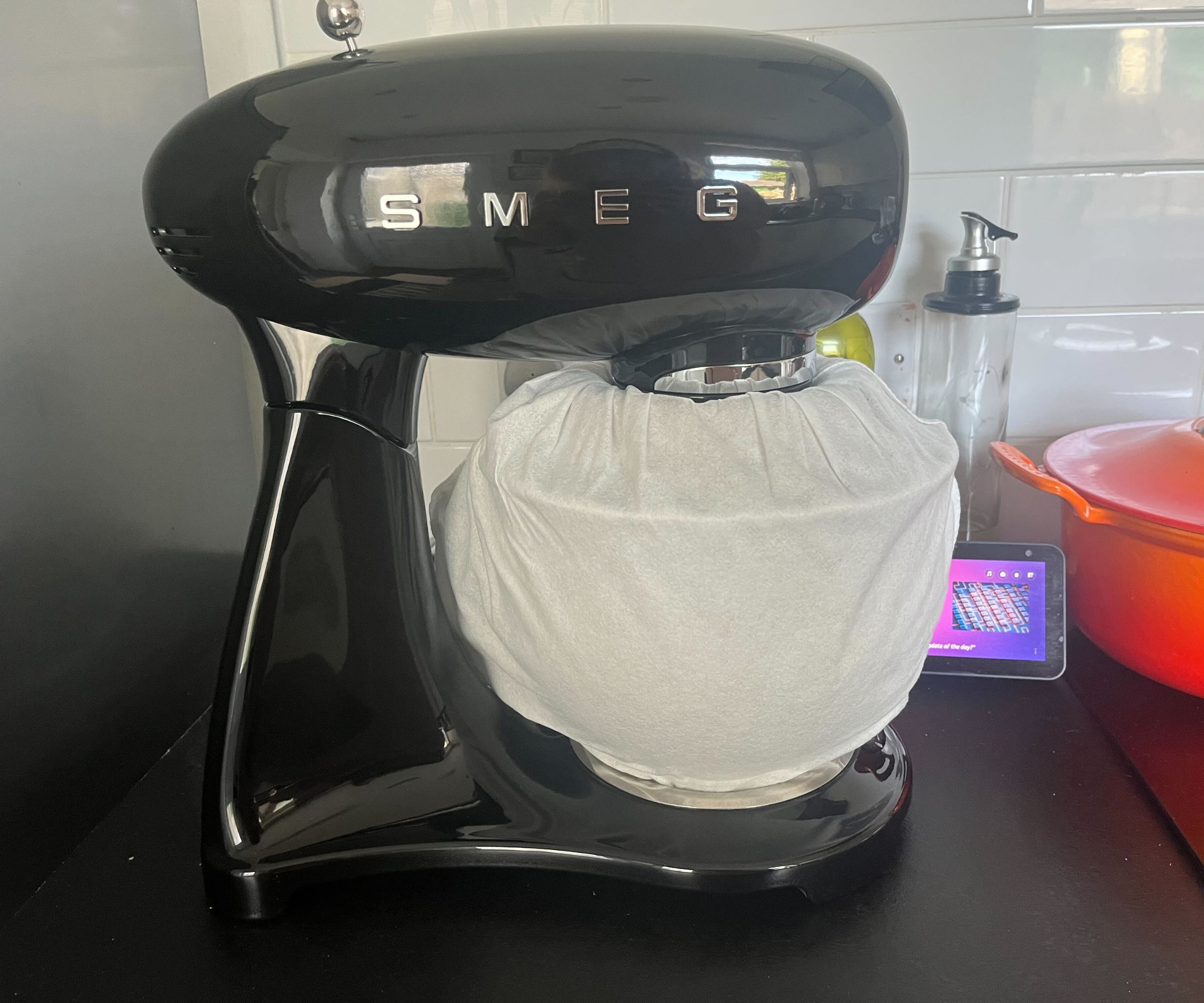 A black SMEG brand stand mixer on a kitchen counter with a bag around the mixing bowl. 