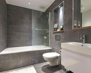 bathroom with grey tiled walls and floor and white wash basin