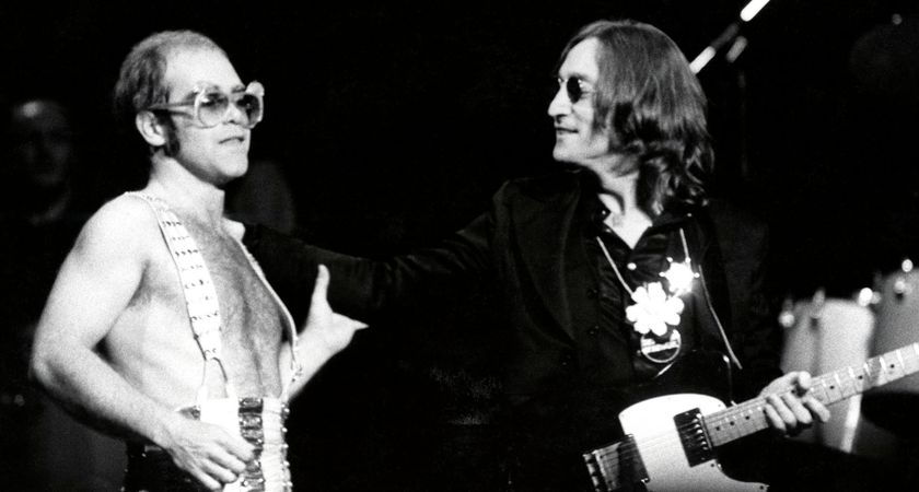 Elton John, bare chested but wearing braces and custom sunglasses, performs with John Lennon at his Madison Square Garden Thanksgiving show in 1974. Lennon plays a Fender Telecaster Deluxe.
