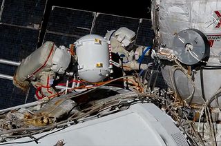 Cosmonauts Sergey Ryzhikov (at left) and Sergey Kud-Sverchkov return a pressurized container with a fluid flow regulator to the Poisk mini-research module during a spacewalk outside the International Space Station on Wednesday, Nov. 18, 2020.