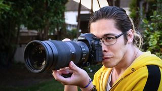 Reviewer holding the Nikon D850 with a telephoto lens attached infront of green foliage