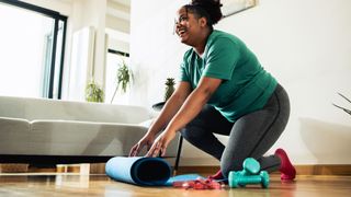 Woman rolling up yoga mat next to dumbbells