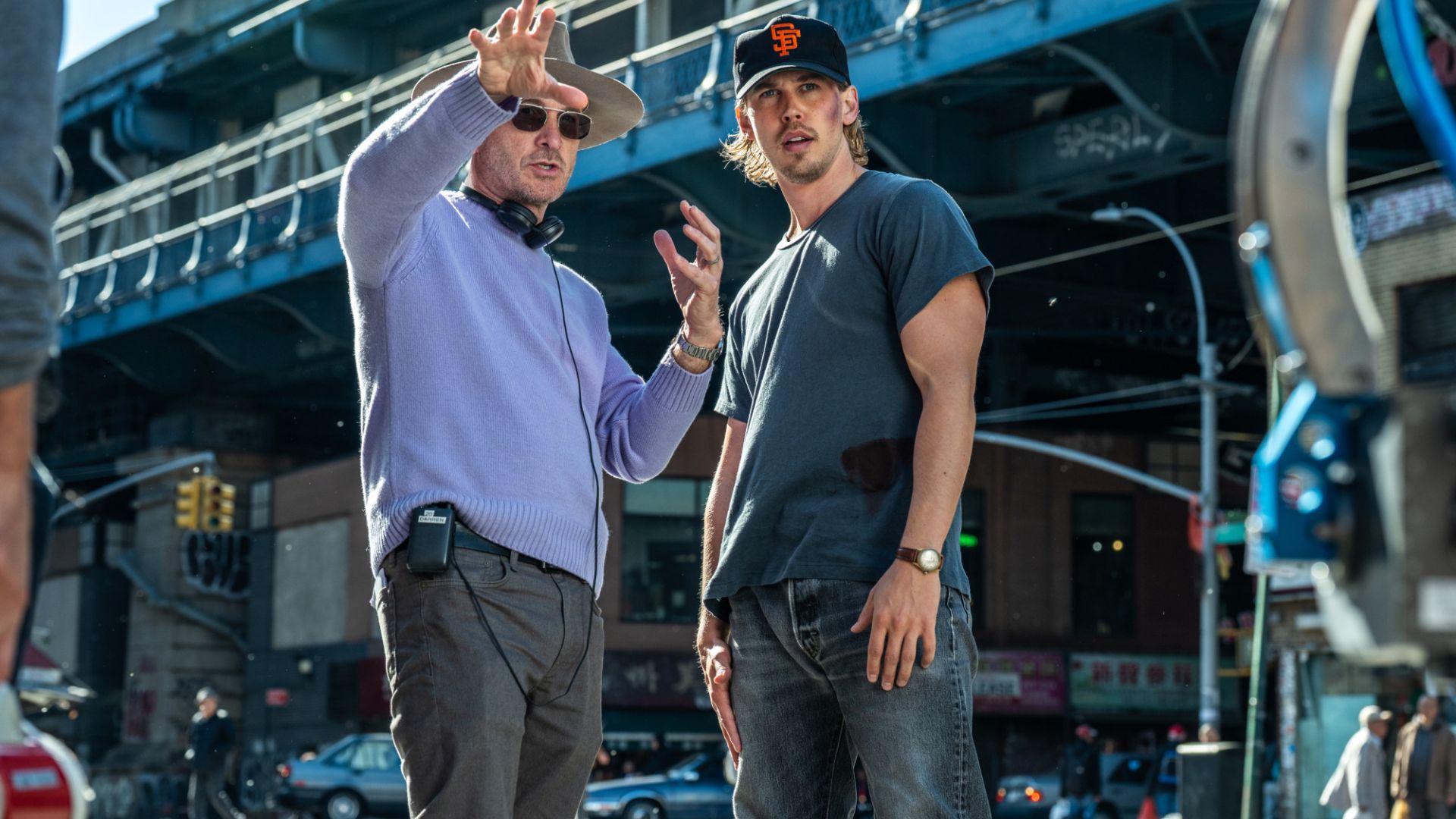 an image of darren aronofsky and austin butler on set of the film caught stealing. Darren is mid conversation with Austin giving him feedback on the scene they are shooting