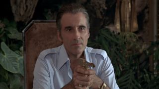Christopher Lee calmly aims his pistol while sitting at the table in The Man with the Golden Gun.