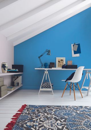 home office in loft with blue feature wall white floorboards white desk and chair