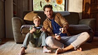 Man and son sitting on the floor in front of the couch with controllers playing video games