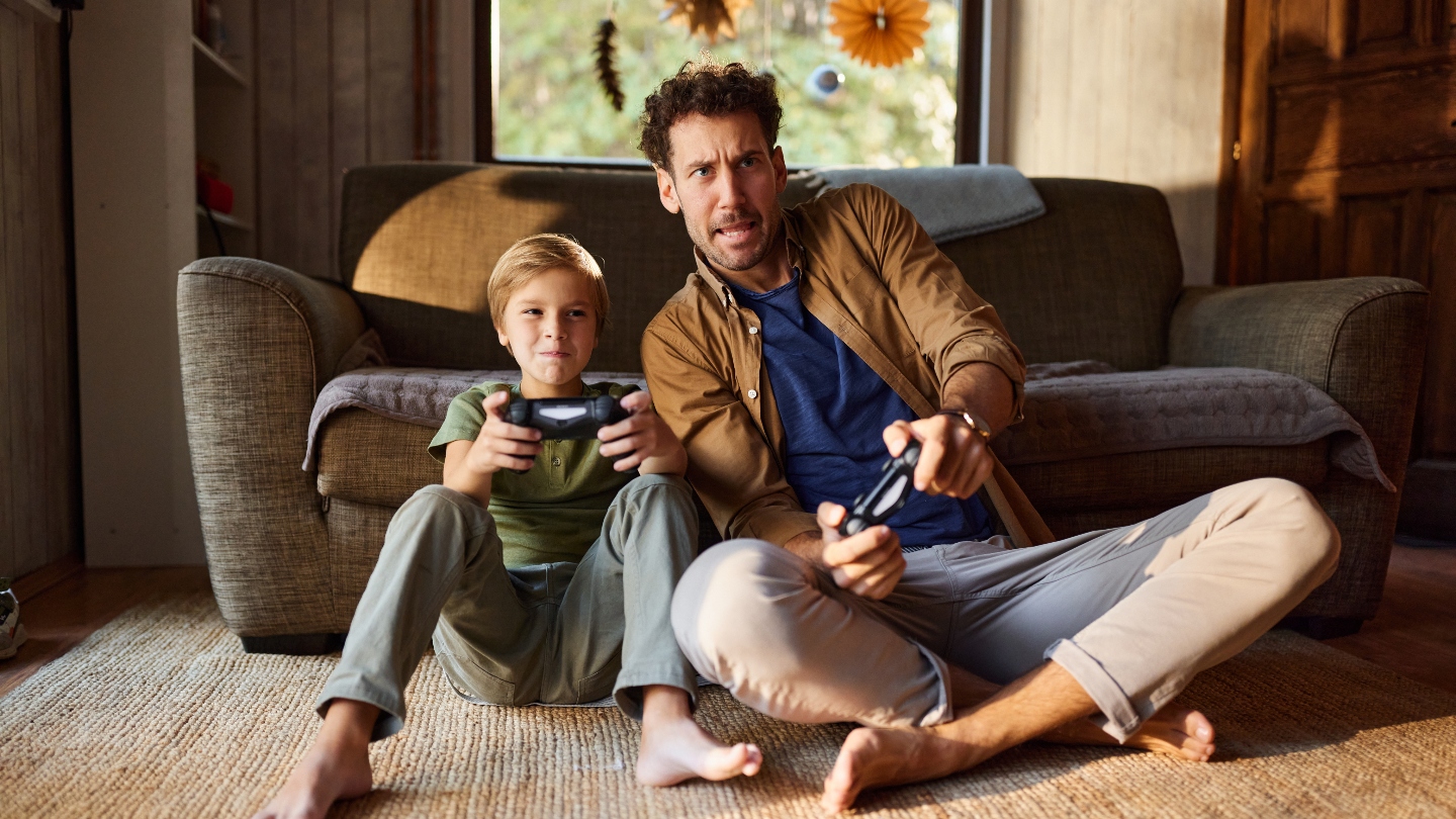 Man and son sitting on the floor in front of the couch with controllers playing video games