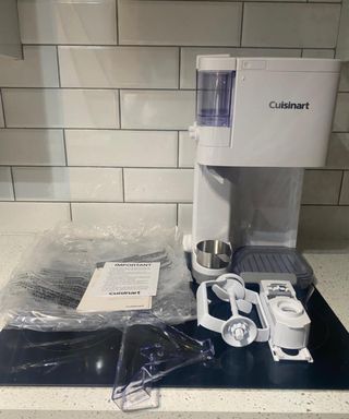 Cuisinart Soft Serve Ice Cream Maker machine with parts, accessories and plastic packaging on induction hob in white tiled kitchen