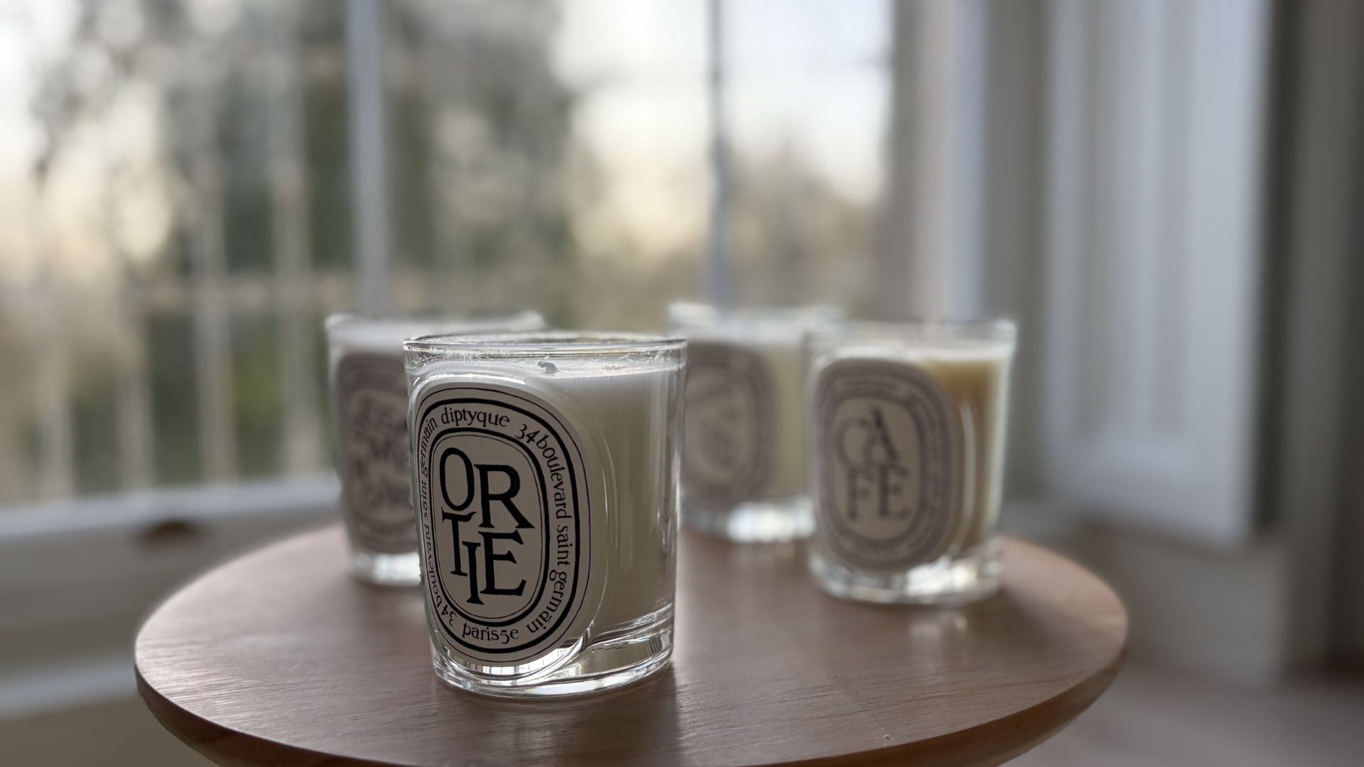 Three of the new Diptyque candles on a table: Ortie, Cafe, and Sesame Noir