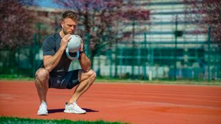 Man holding a kettlebell doing a squat outdoors on a running track