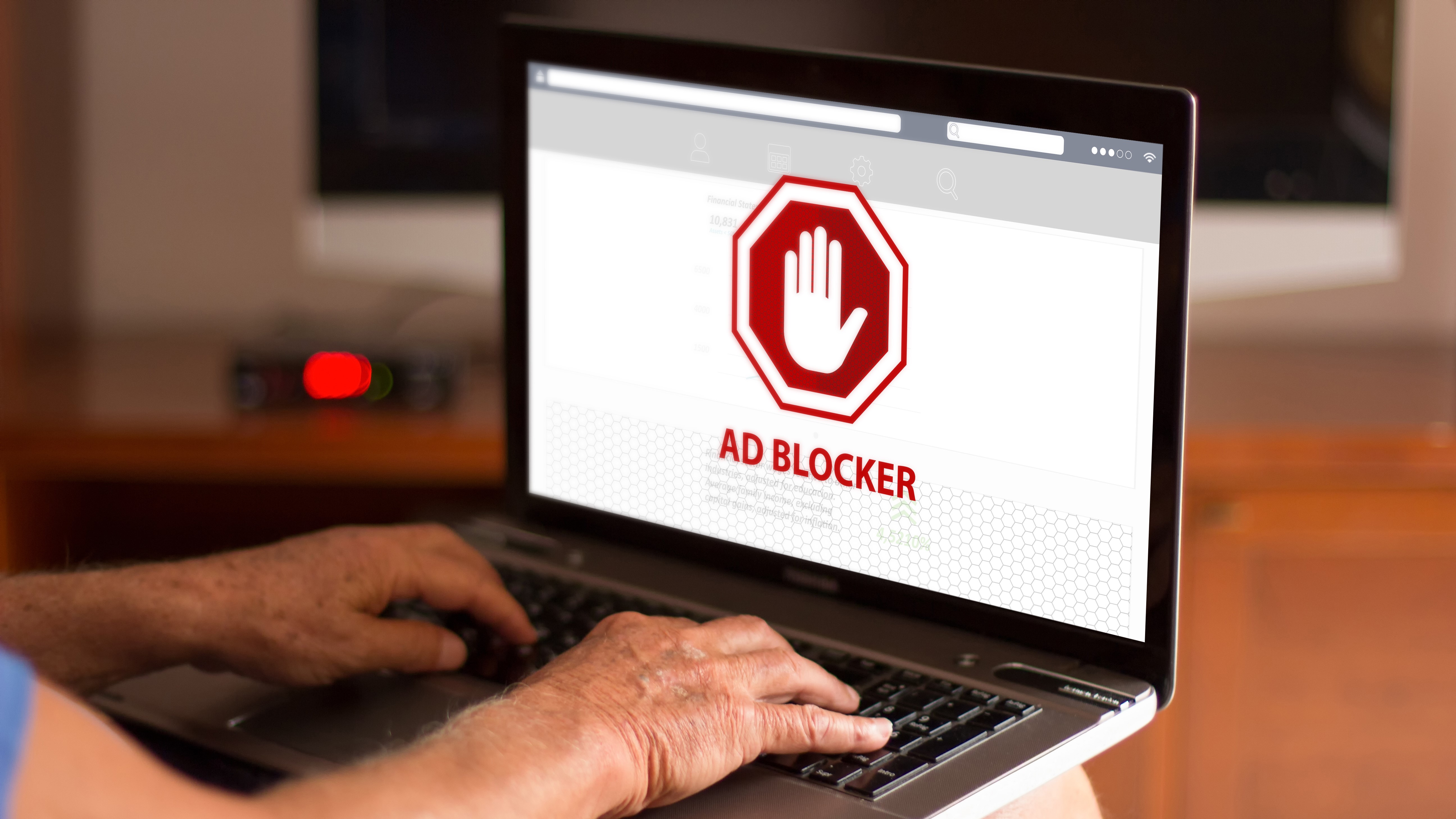 A laptop displaying a red hexagon with a white hand in it, with text underneath it that reads 'ad blocker'