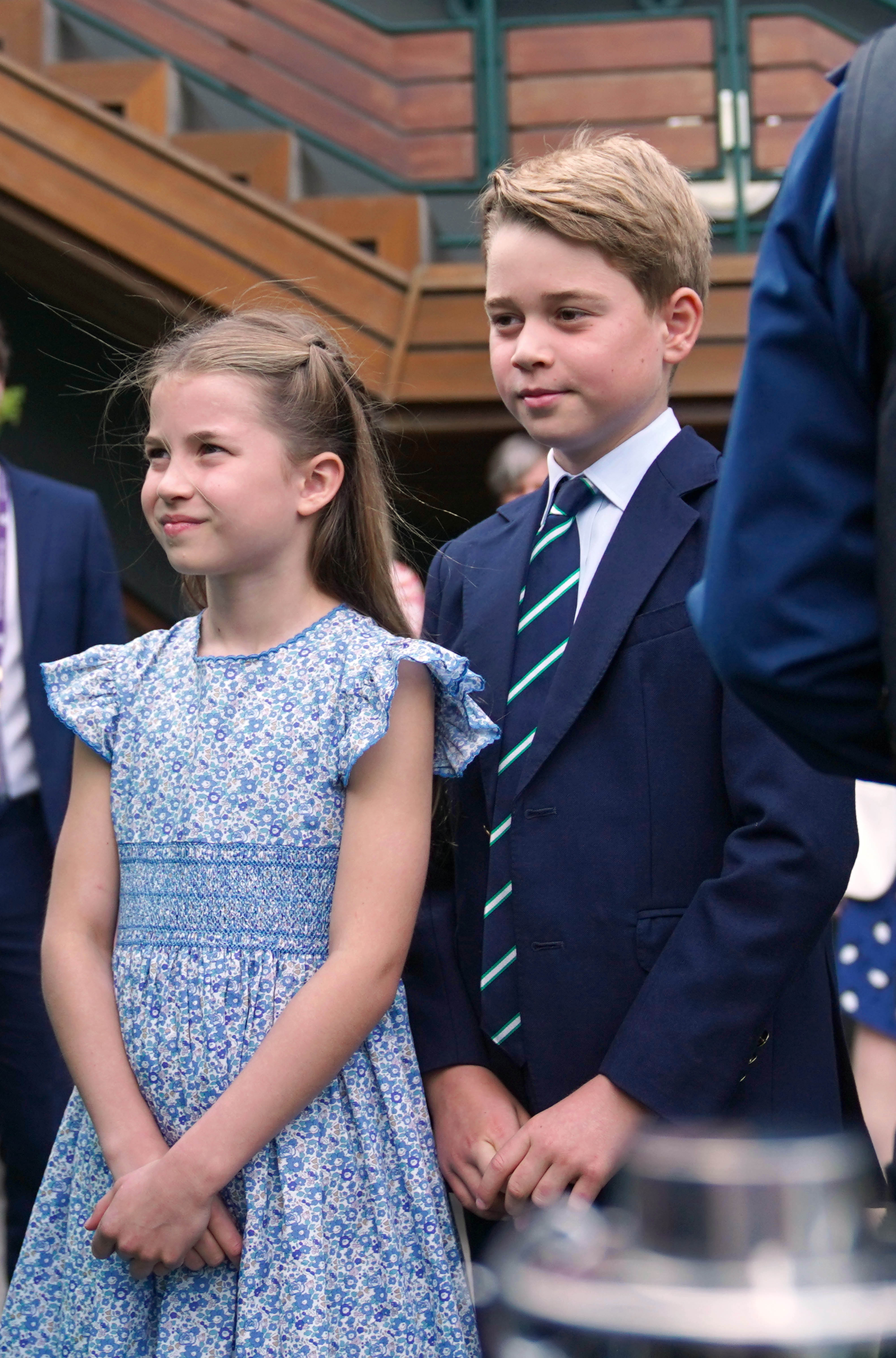 Princess Charlotte wearing a blue floral dress standing next to Prince George in a suit at Wimbledon 2023