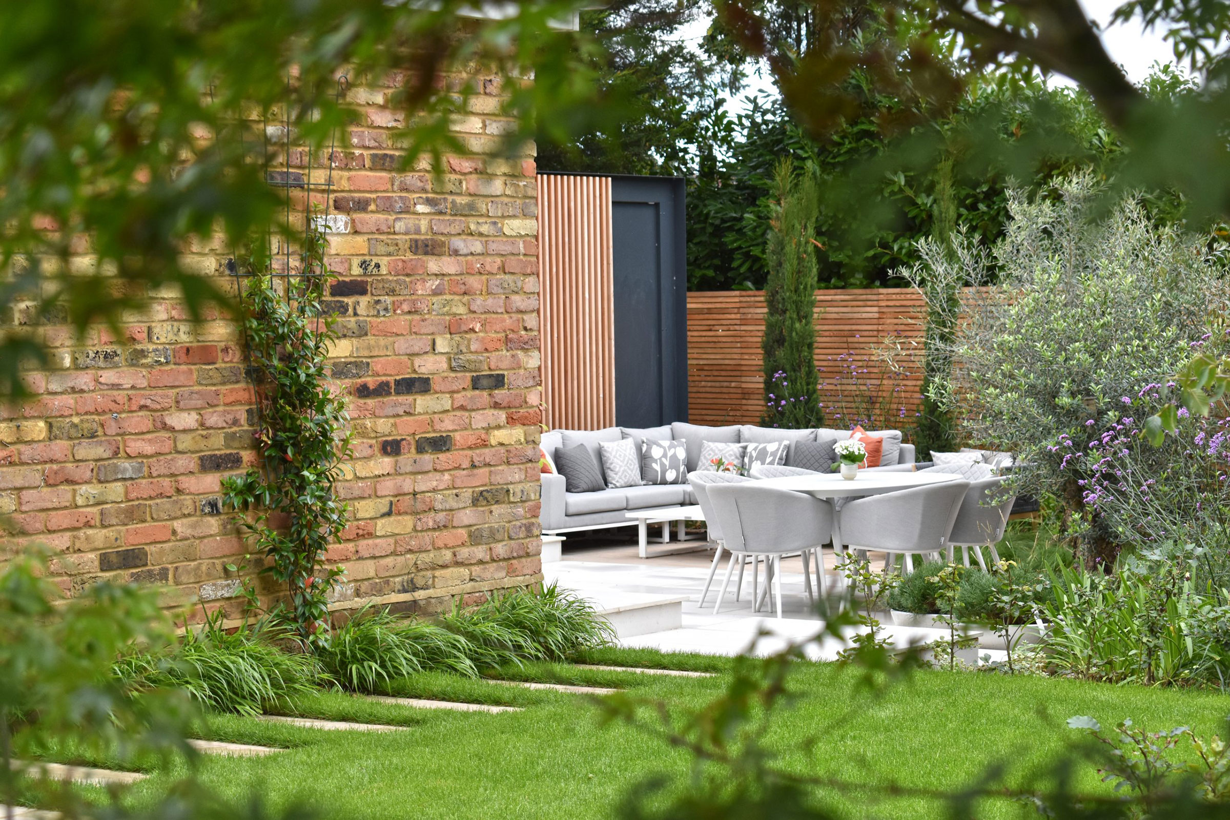 Curated yard space with neat garden, surrounding planting, decking space and slat patio furniture