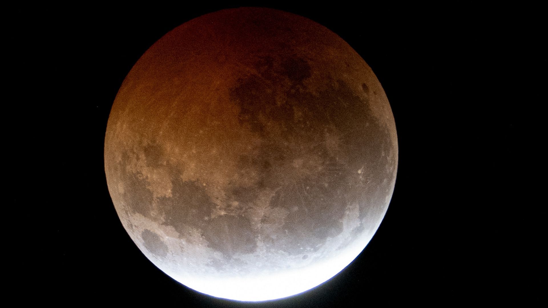 A full moon is photographed during a lunar eclipse, as Earth's shadow darkens the lunar disk in a black sky.