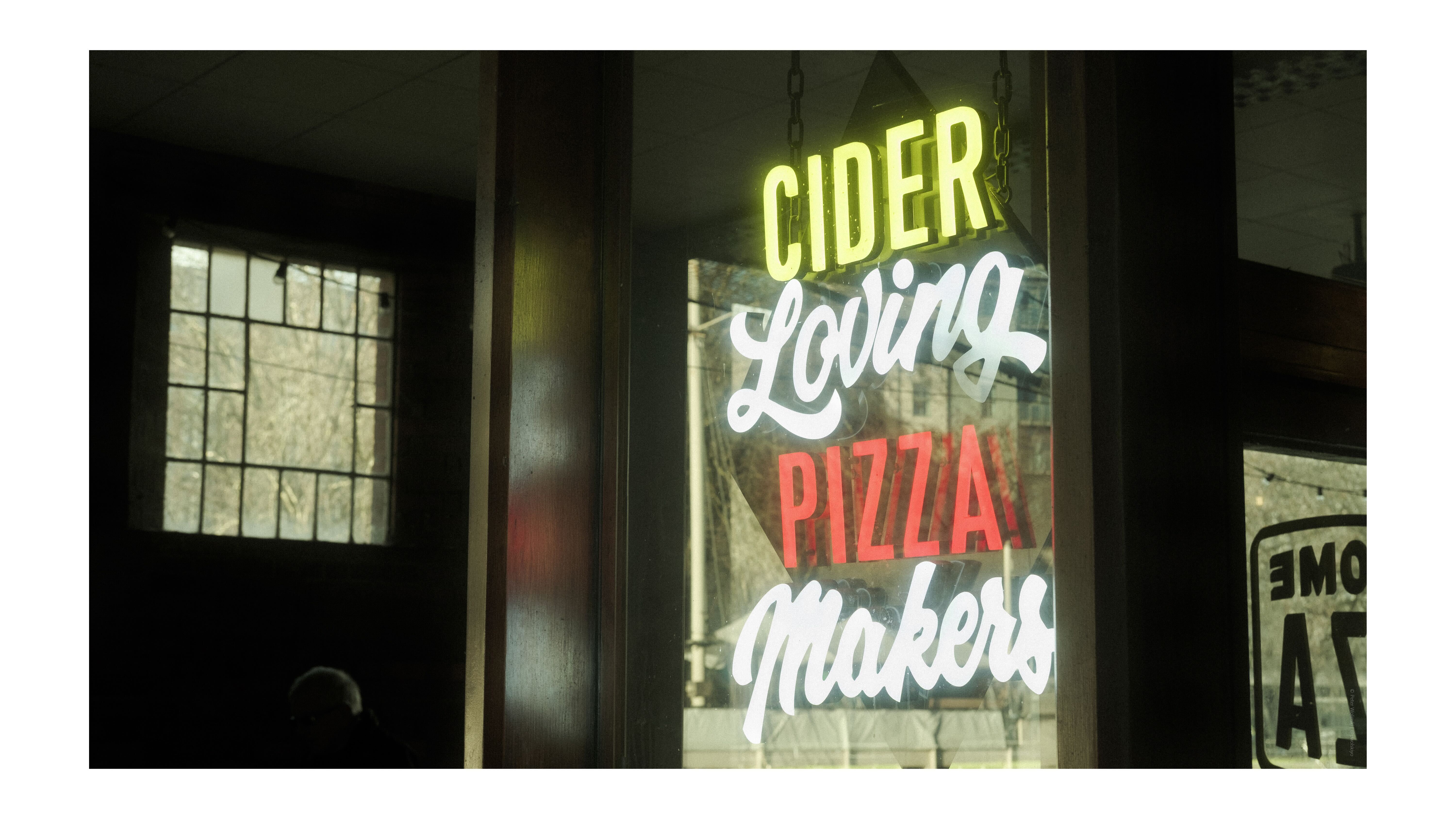 A bright neon sign advertising pizza and cider, taken on the Fujifilm X-E4