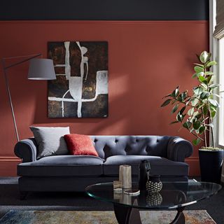 A red living room with black painted above picture rail and dark upholstered sofa