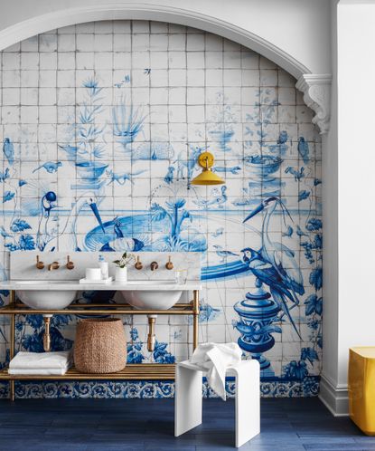 A bathroom backsplash idea with painted blue and white tiles depicting a landscape mural across alcove wall