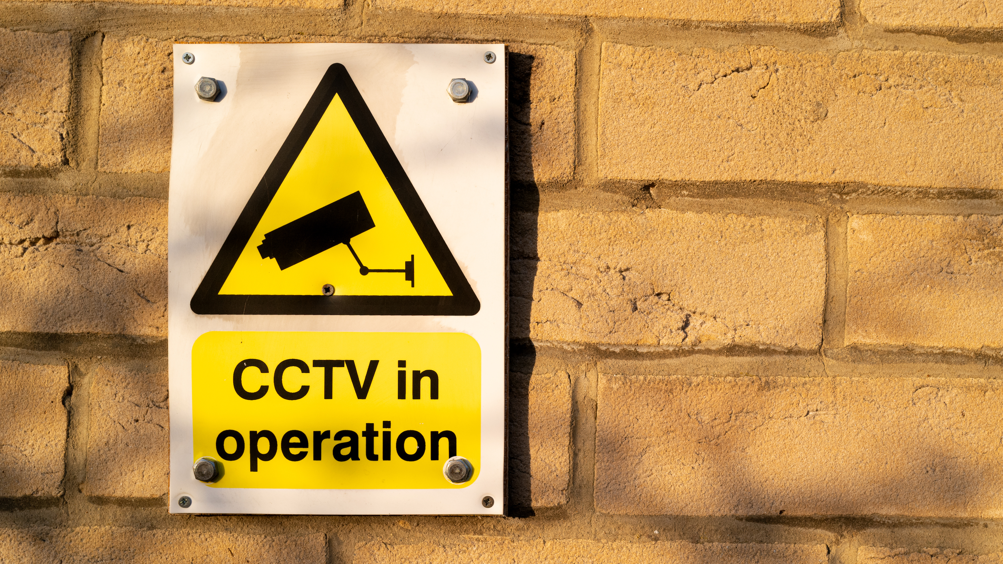 Light coloured brick wall detail of house with CCTV in operation sign attached