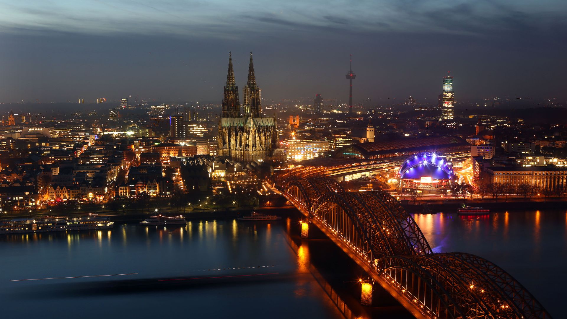 Picture shows a ship making its way over the river Rhine and passing under the Hohenzollern bridge in Cologne. In background you can se the city's landmark, the Cologne Cathedral