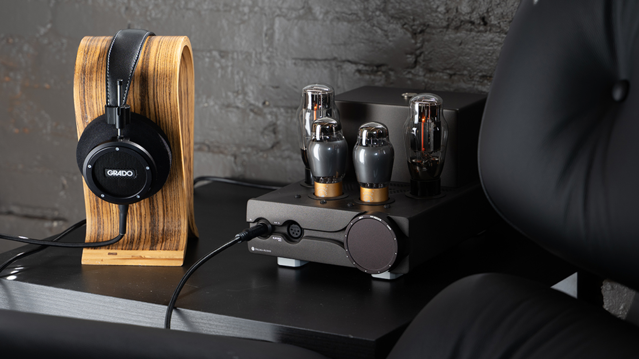 The Grado Signature S750 headphones on a wooden stand next to a dark headphone amp with large valves protruding from the top