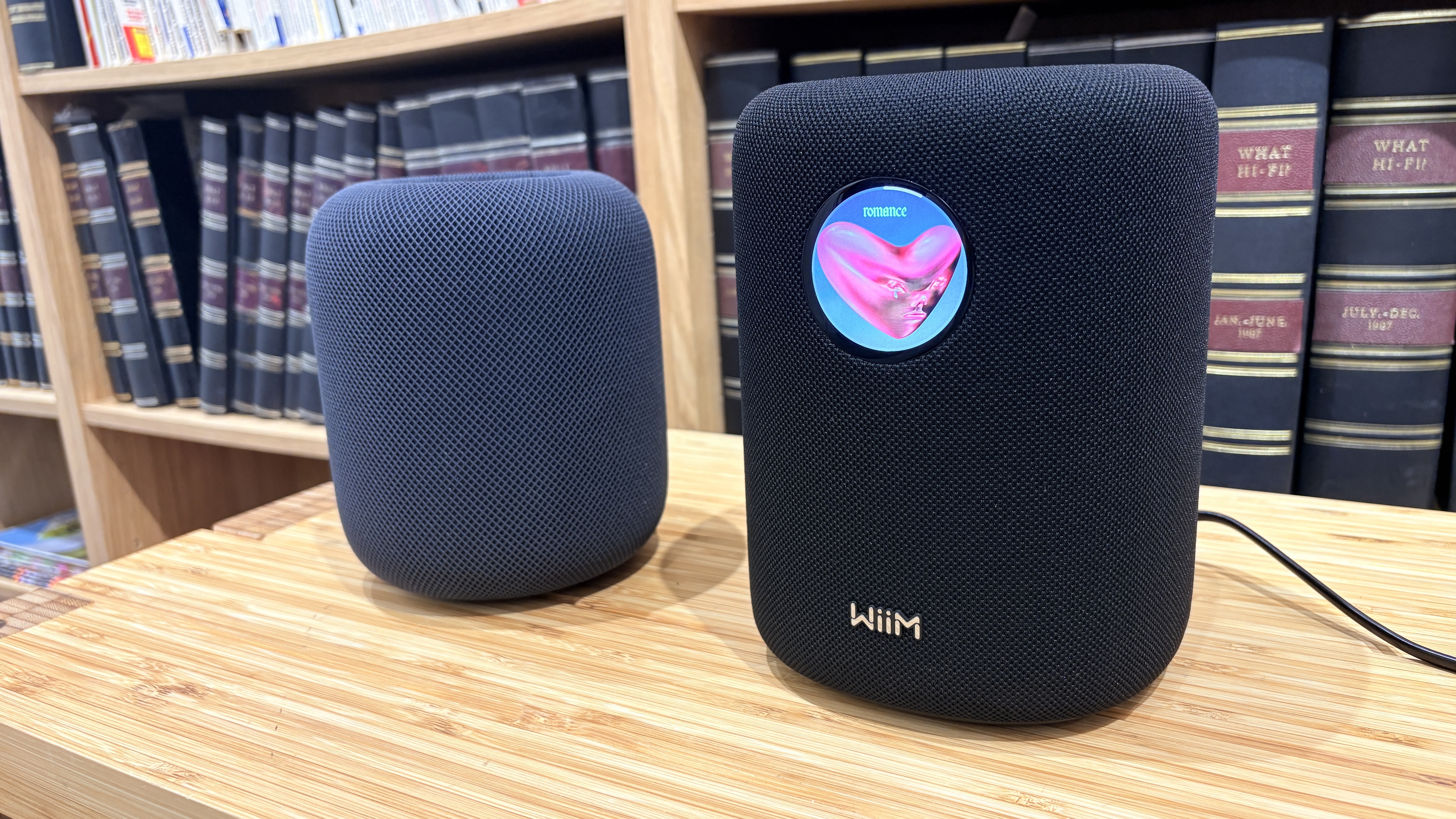 A black Apple HomePod 2 next to a black WiiM Sound on a wooden surface