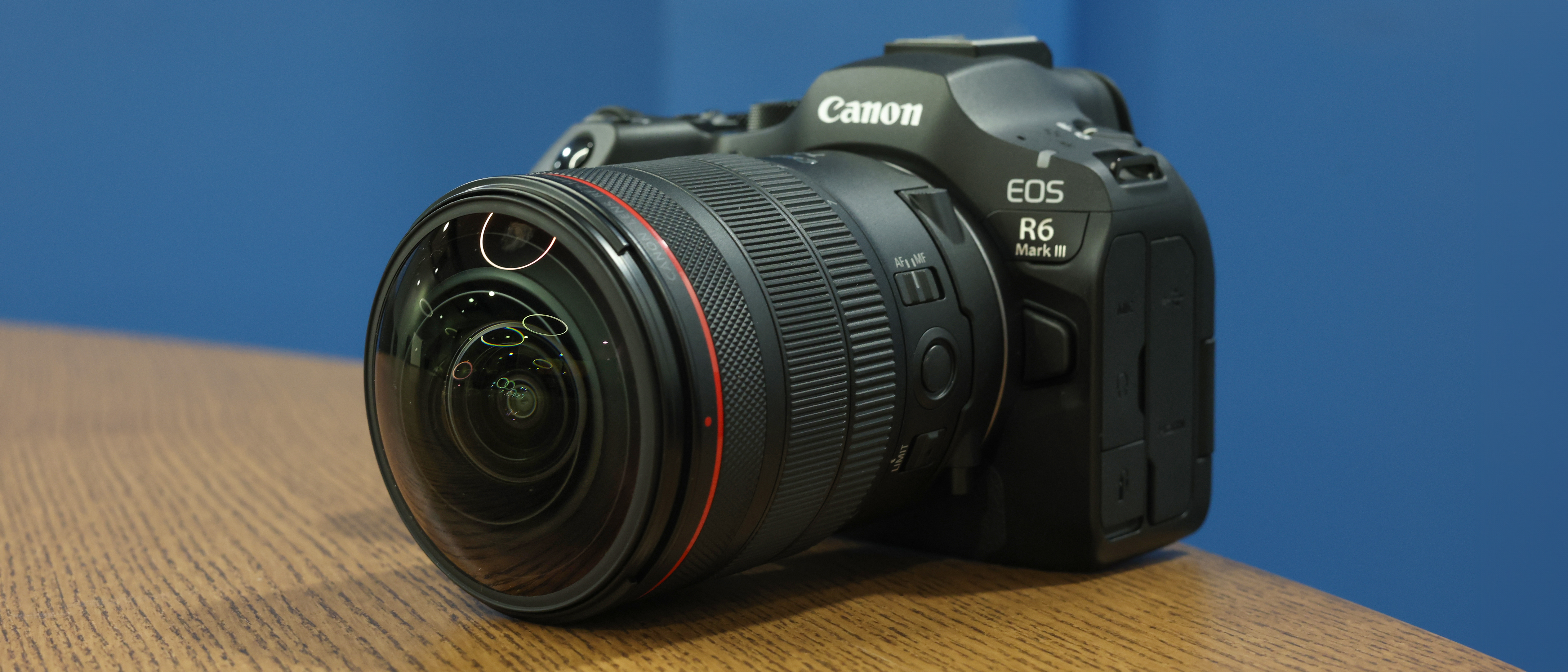 Canon RF 7-14mm f/2.8-3.5L Fisheye STM on a wooden surface in front of a blue background
