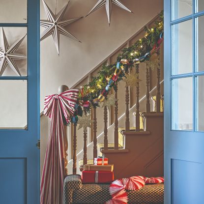 A staircase decorated for Christmas with a garland, a paper chain, a striped XL Christmas bow and three striped paper Christmas stars