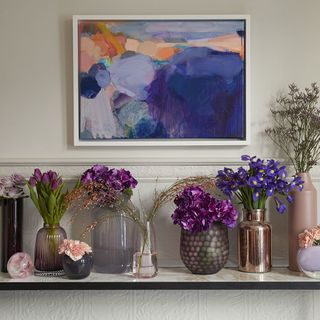 room with photoframe on wall violet flower in glass vase and blue fower in copper vase