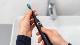 person using a black electric toothbrush at the bathroom sink