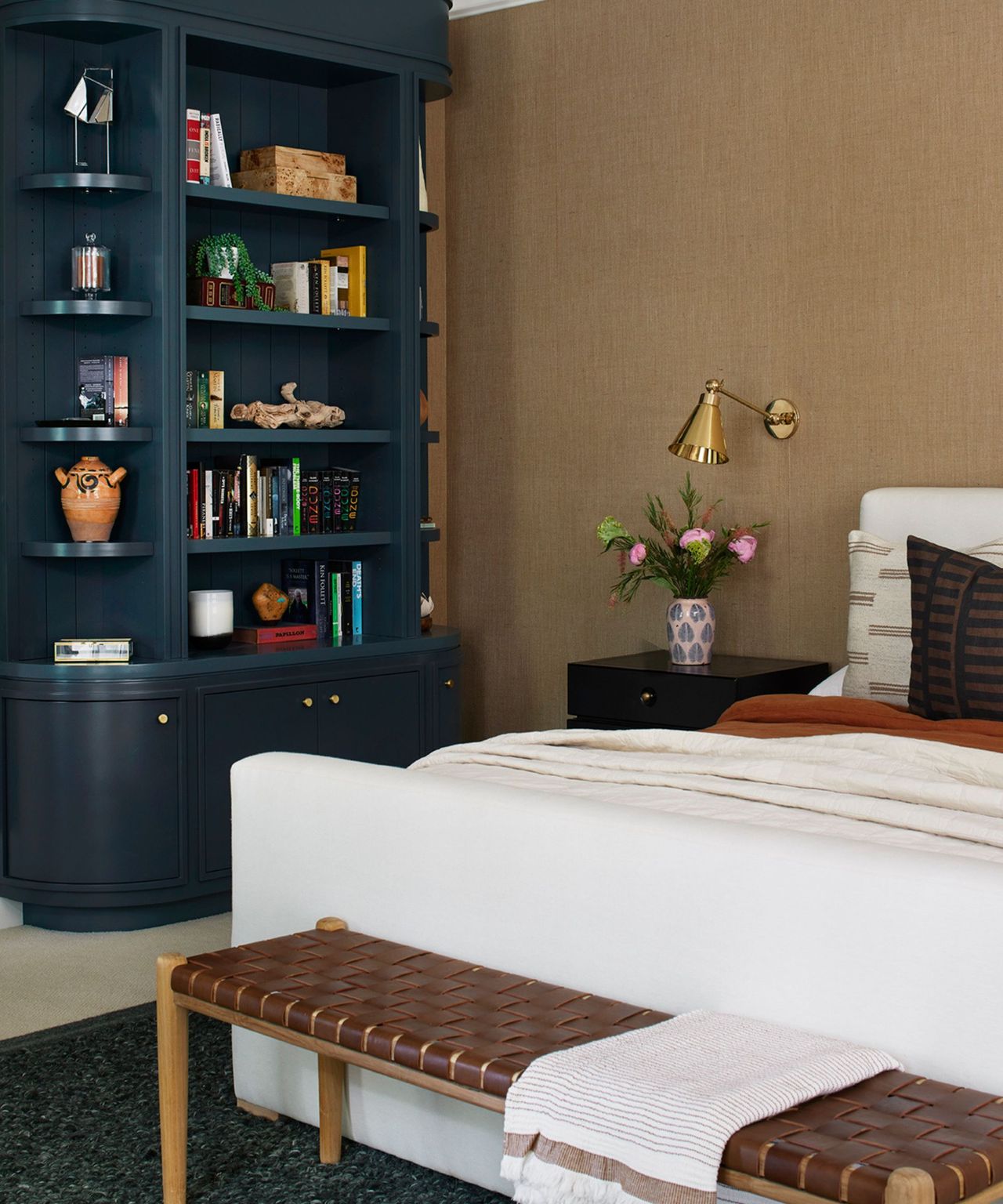 A tan bedroom with textured wallpaper, a built-in blue bookshelf, and bench