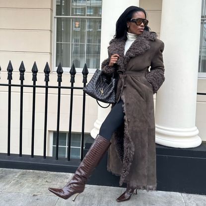 @nlmarilyn wearing a brown fur coat, black leggings and brown knee-high boots