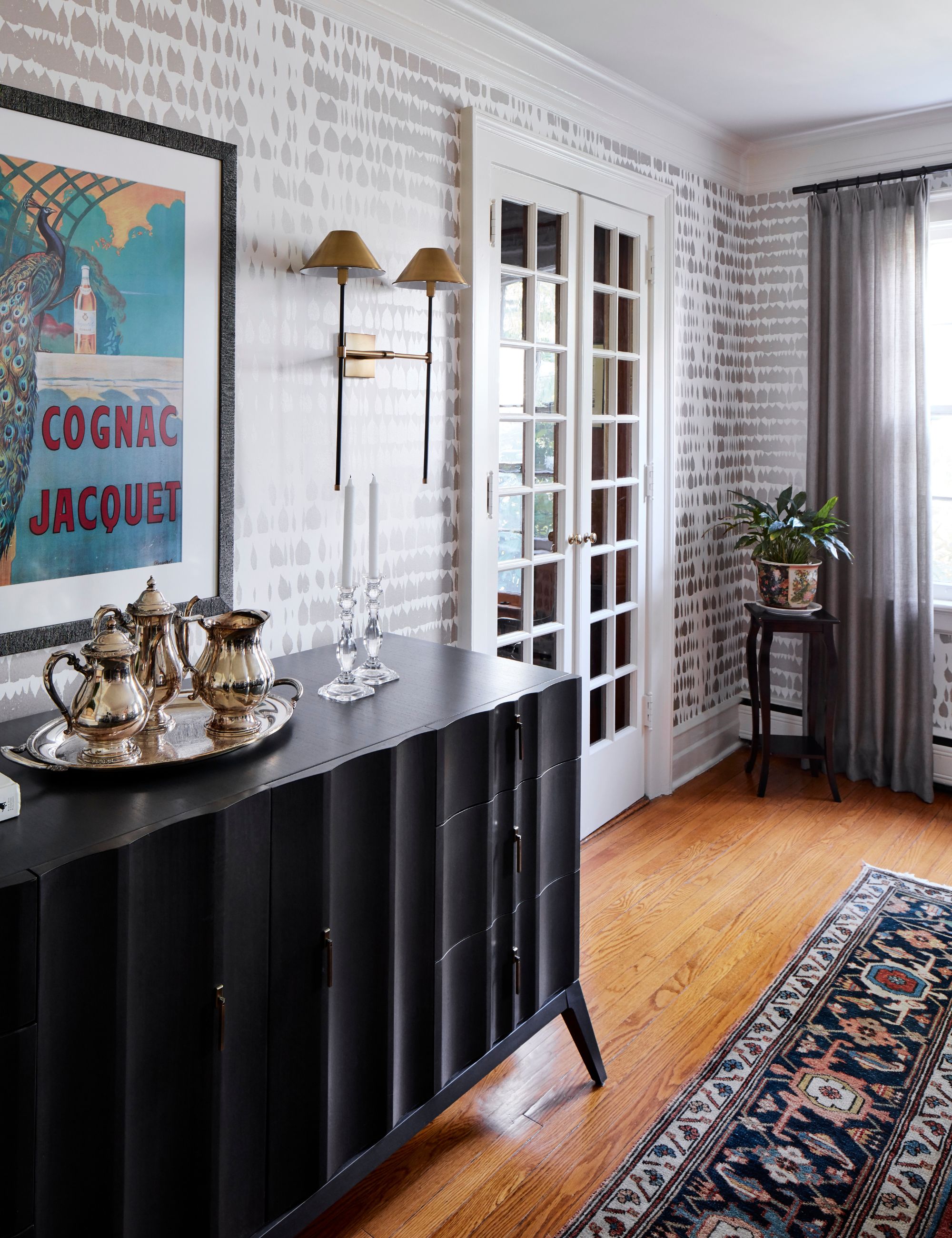 Black sideboard in a dining room with gray and white wallpaper and frame print