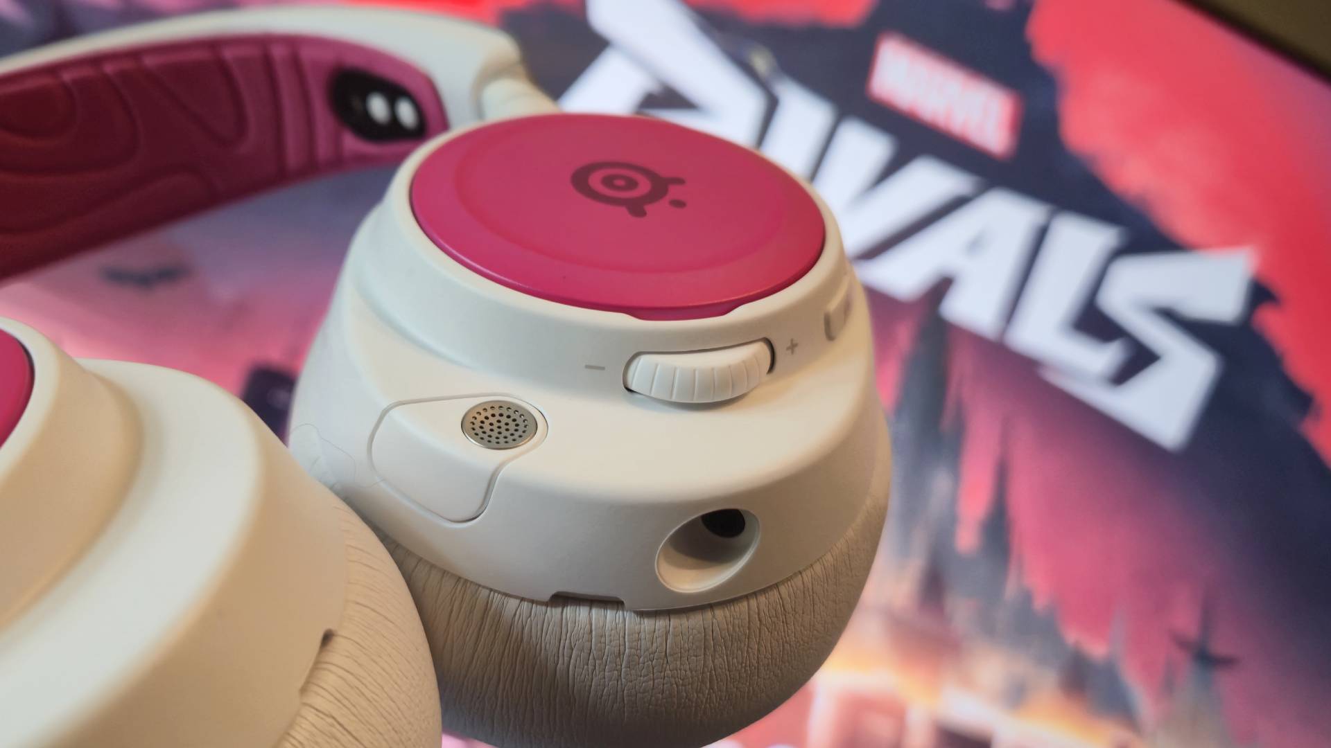 Photo of a white headset with pink covers in the foreground, and a screen running Marvel Rivals in the background.