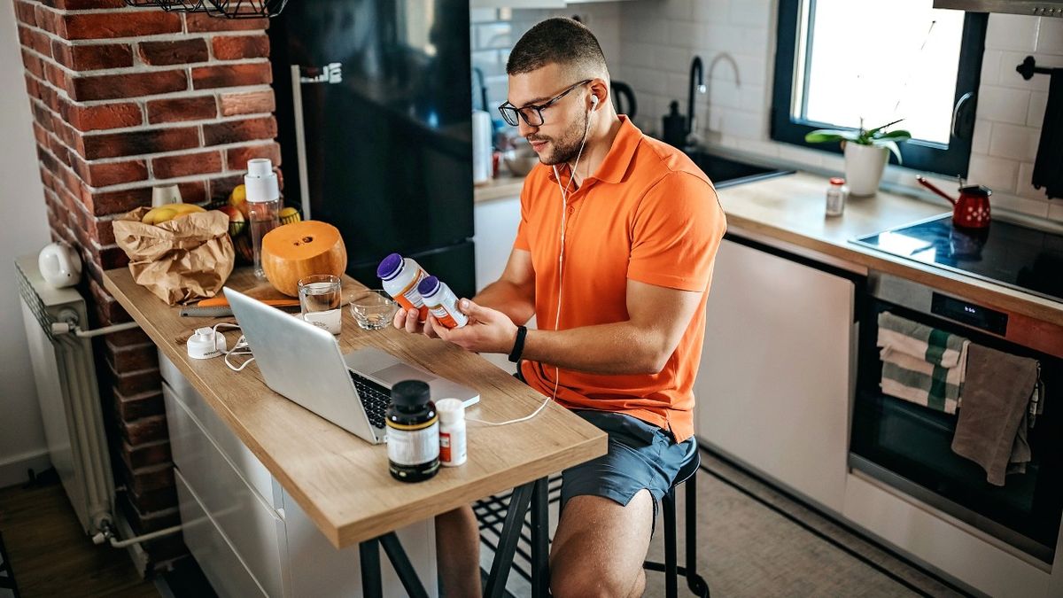 Man sitting at kitchen island examining supplement bottles