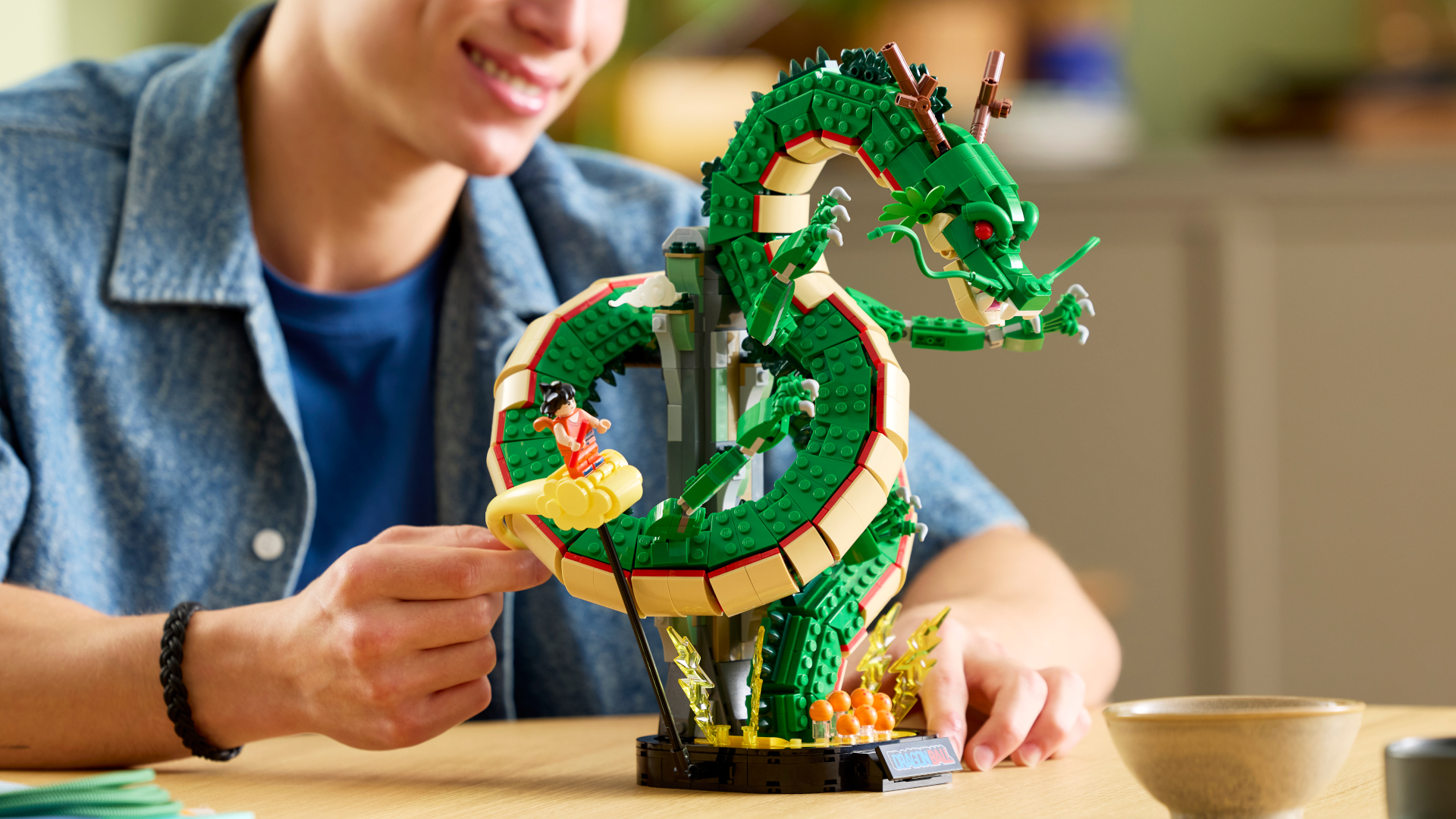A man smiles while moving the Lego Shenron &amp; Goku set