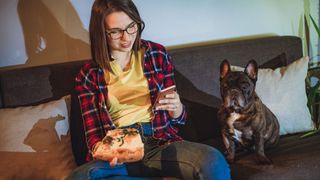 Woman eating pizza on the sofa with a dog next to her