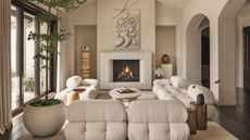 beige living room with fluted fireplace, sculptures, arched doorways, potted tree, beige modular sofas, and round white coffee table on a beige rug