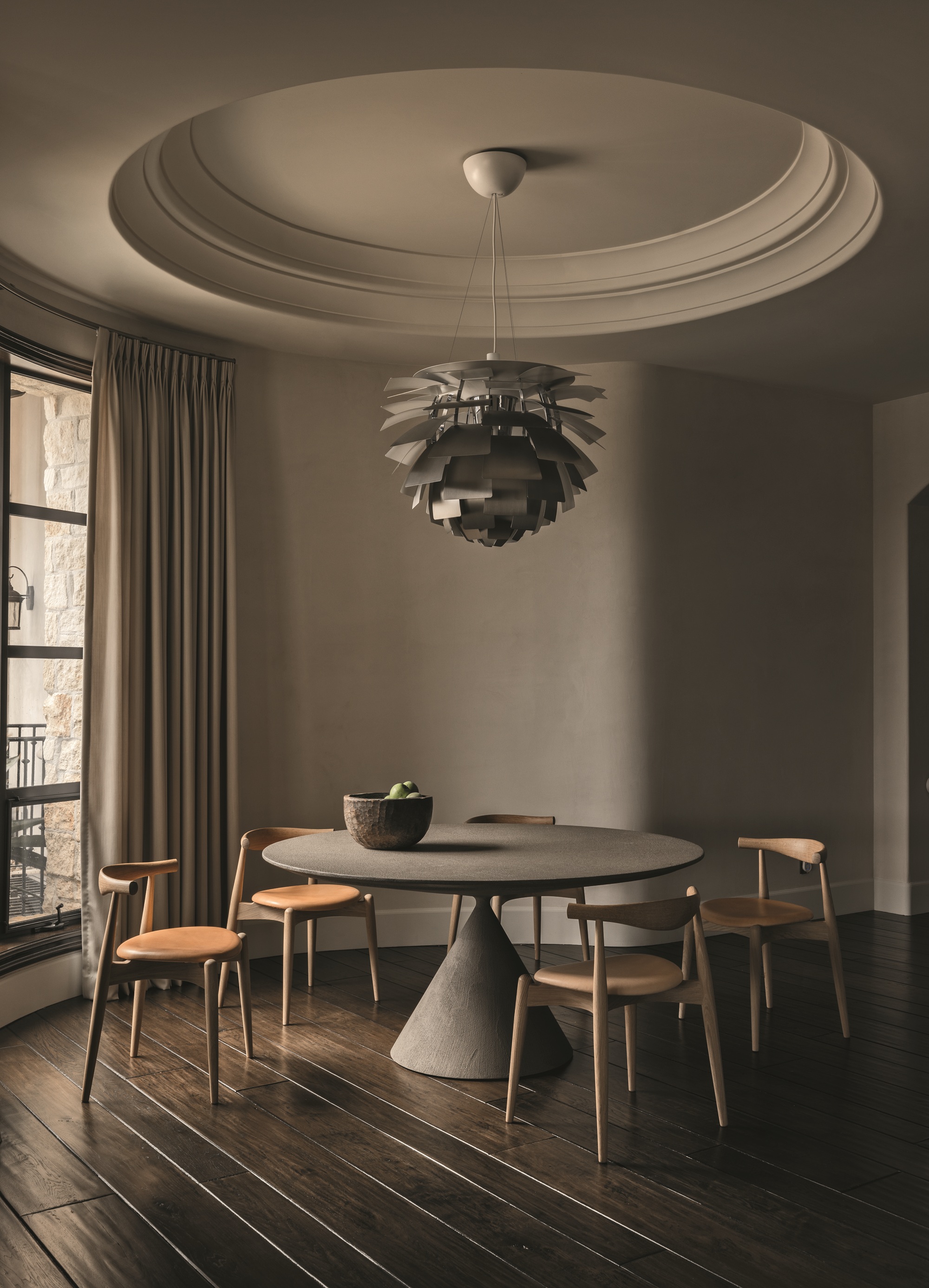 modern dining room with round table with timber chairs, dark timber floorboards, curved wall, louis poulsen artichoke lamp hanging over the table, and carved round detail on the ceiling