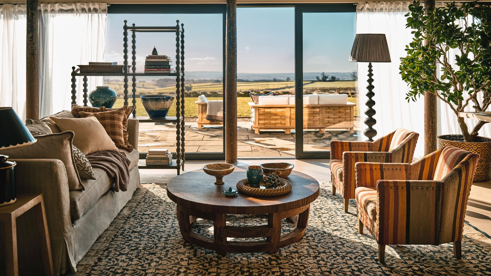 A maximalist living room with floor to ceiling glass doors out onto a patio with wicker outdoor furniture. 