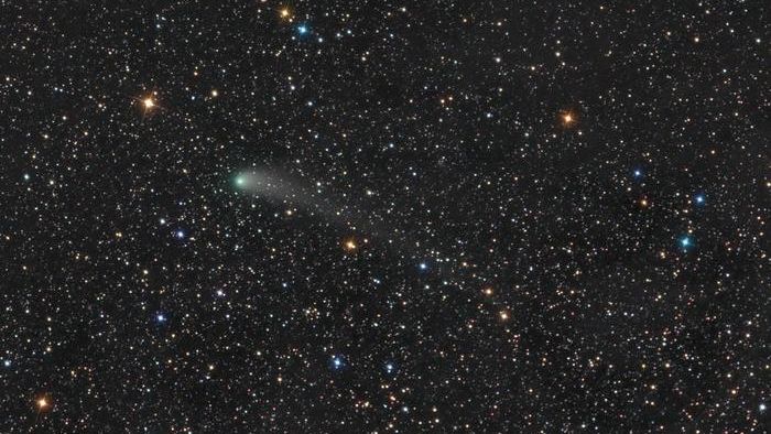 the black of space is filled with stars of varying size and brightness. near the center, a larger green star is actually a comet and has a faint green tail to the right.