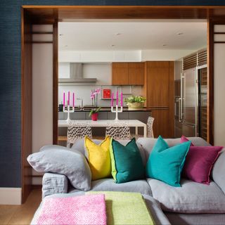 open plan living room kitchen area with bright cushions on sofa, white dining table and chairs in kitchen, bright pink candles